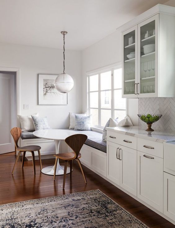 white dining space and kitchen // globe pendant light // hardwood floors // corner bench // white cabinets